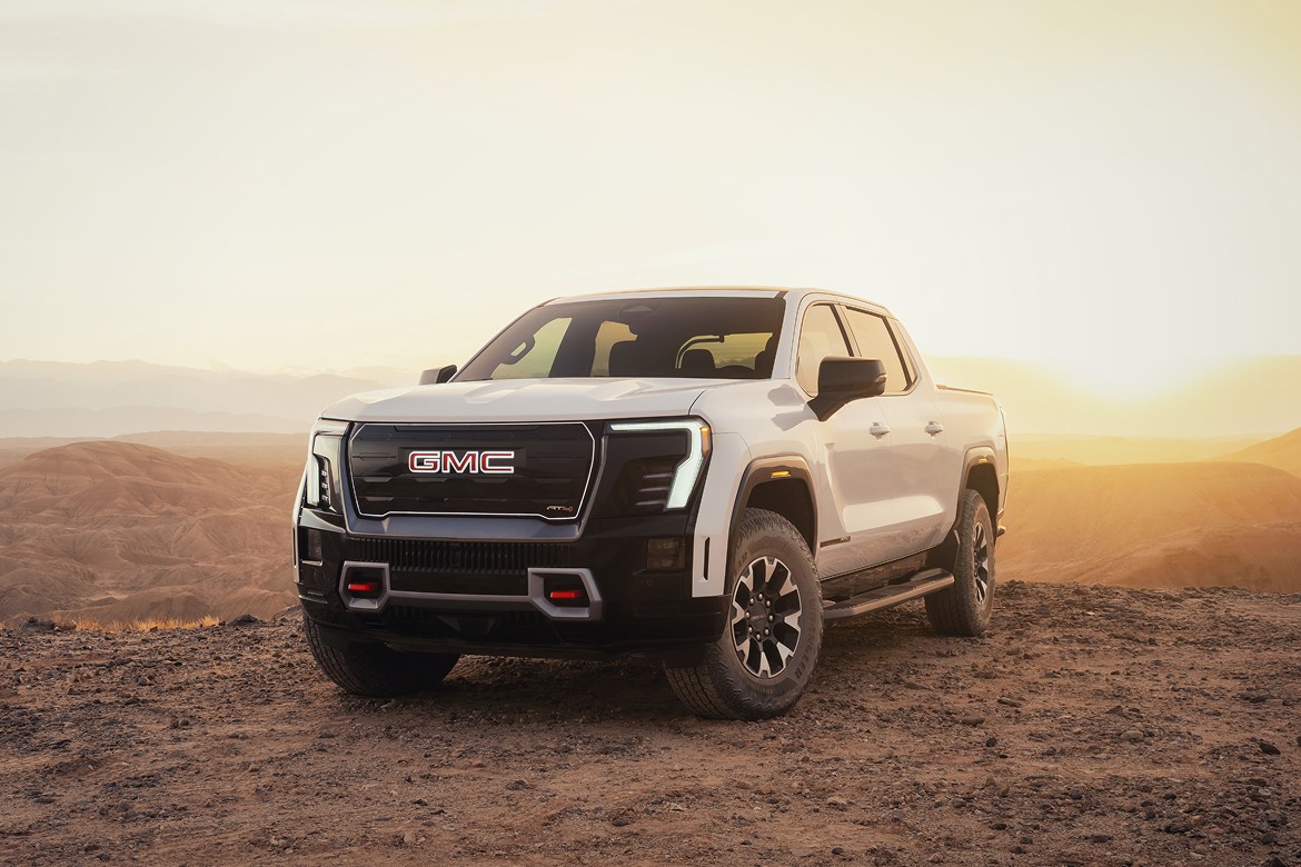 2026 GMC Sierra EV Denali at sunset, front three-quarter view in open landscape with signature LED lighting.
