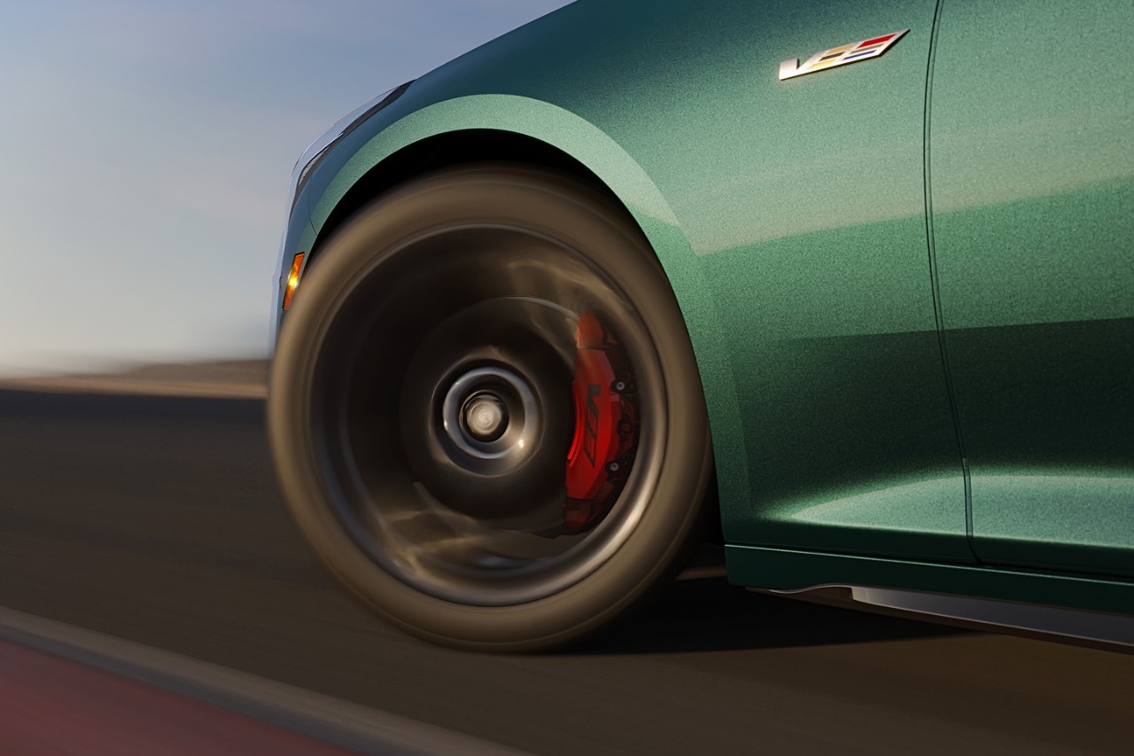 Close-up of green 2025 Cadillac CT5-V wheel in motion on track, showing red Brembo brake calipers and V-Series badge.
